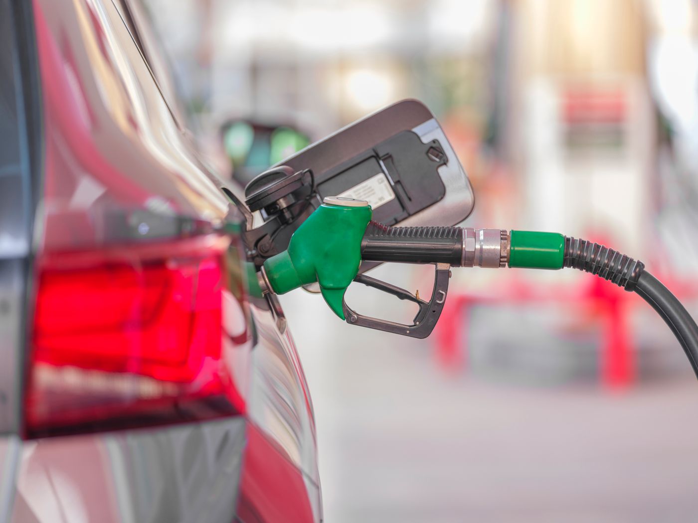 A green fuel pump nozzle refuelling a car on a filling-station forecourt